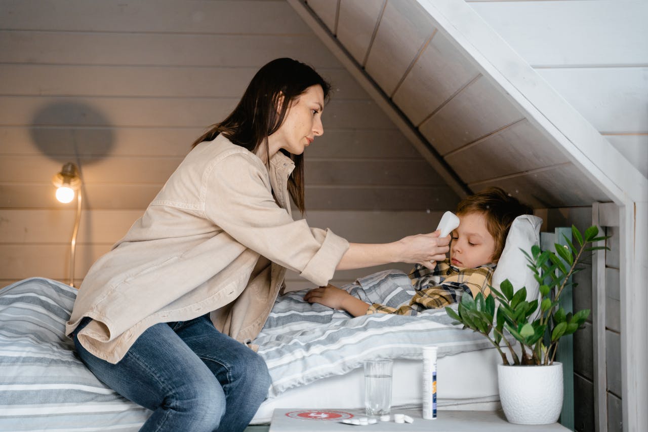 A mother checks her sick child's temperature in a cozy bedroom setting, showcasing care and parenting.
